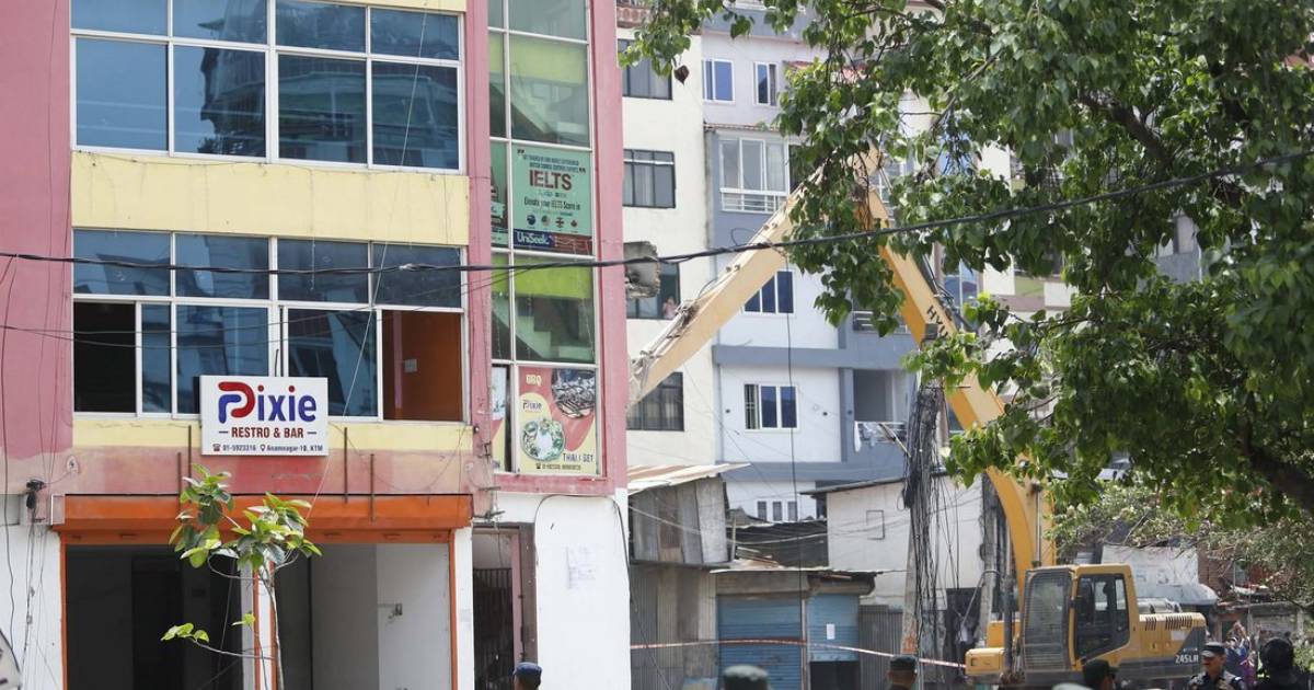 Excavator demolishing part of a multi-storey building in Anamnagar Kathmandu during enforcement action
