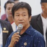 Harka Sampang speaks into a microphone inside Parliament as officials look on